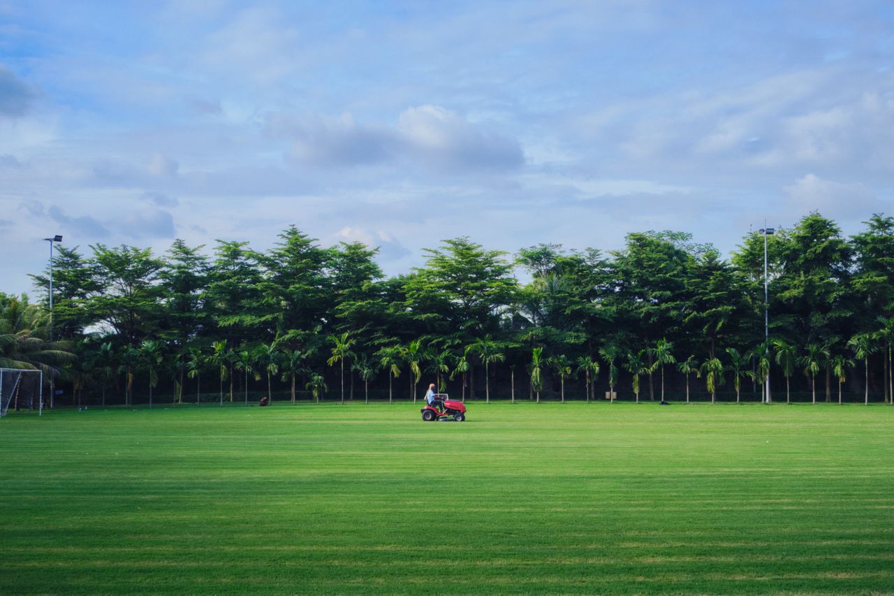 A man mowing the grass on a pristine golf course in Dhaka, Bangladesh, under a clear summer sky.
