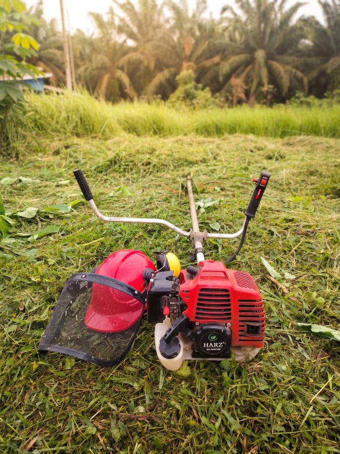 Lawn mower with safety helmet in an outdoor setting, palm trees in Malaysia.